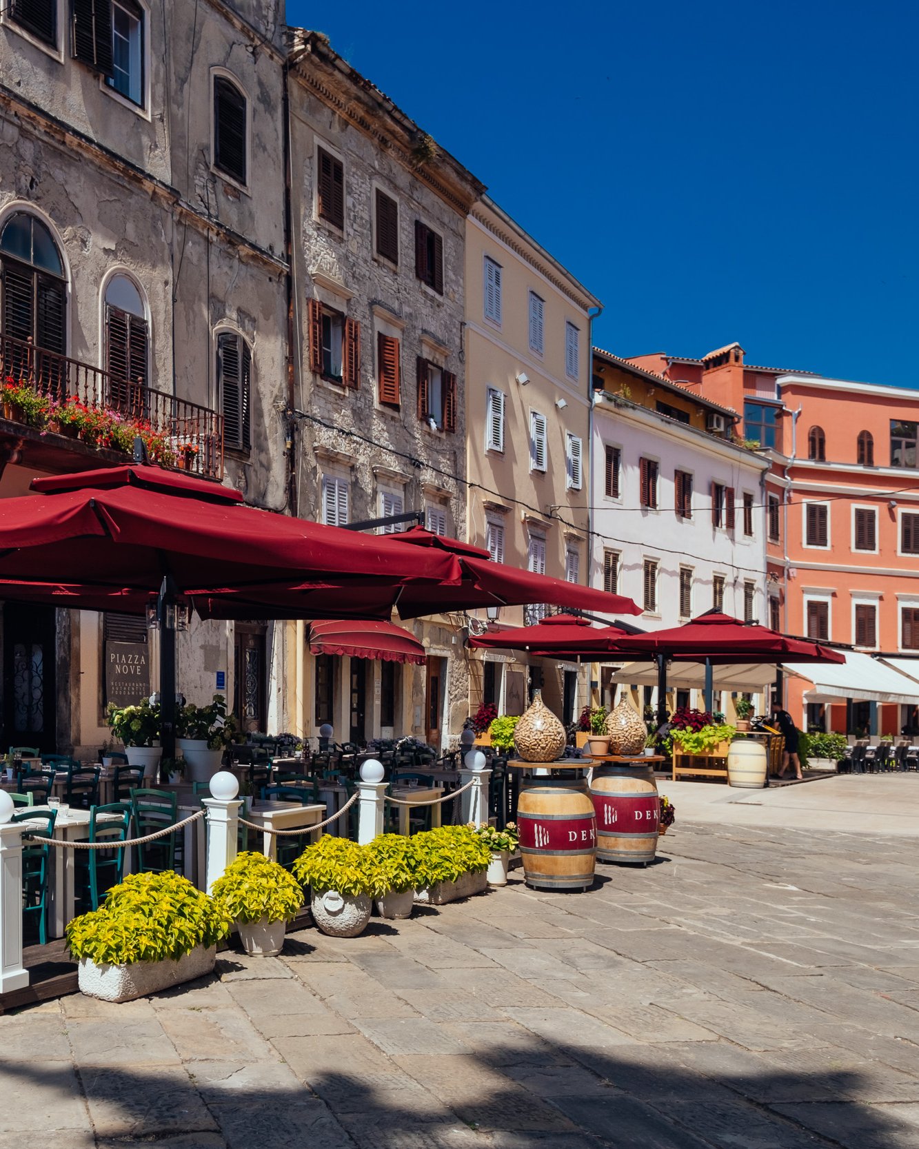 Piazza Nove terrace under dark-red parasols on Kapitolinski trg, Pula, with the old town street beyond